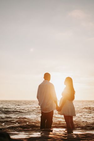 Silhouetted couple holding hands against sunset ocean backdrop.