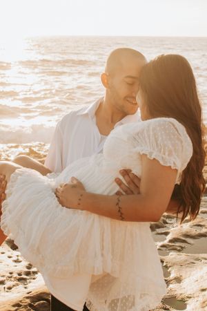Romantic couple embracing on beach rocks during sunset.