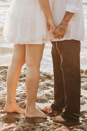 Close-up of couple's legs standing on rocky beach showing matching tattoos.