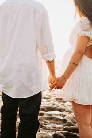 Close-up of couple holding hands on rocky beach during sunset.