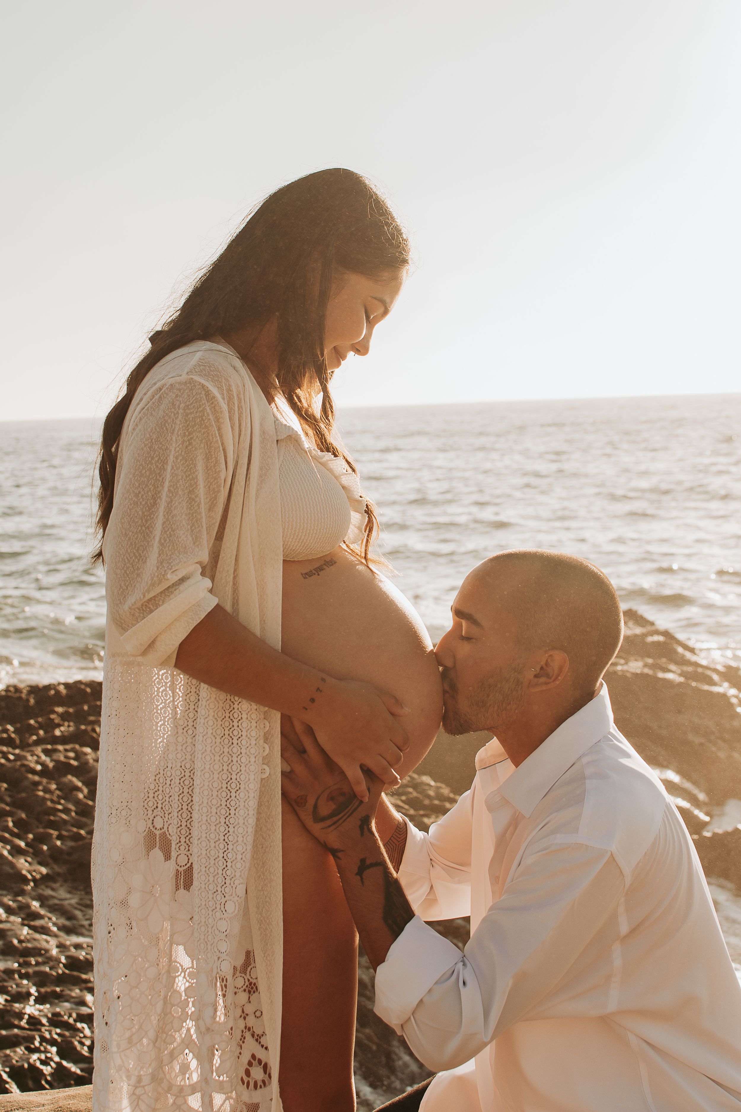 Romantic maternity photo of couple on beach during golden hour.