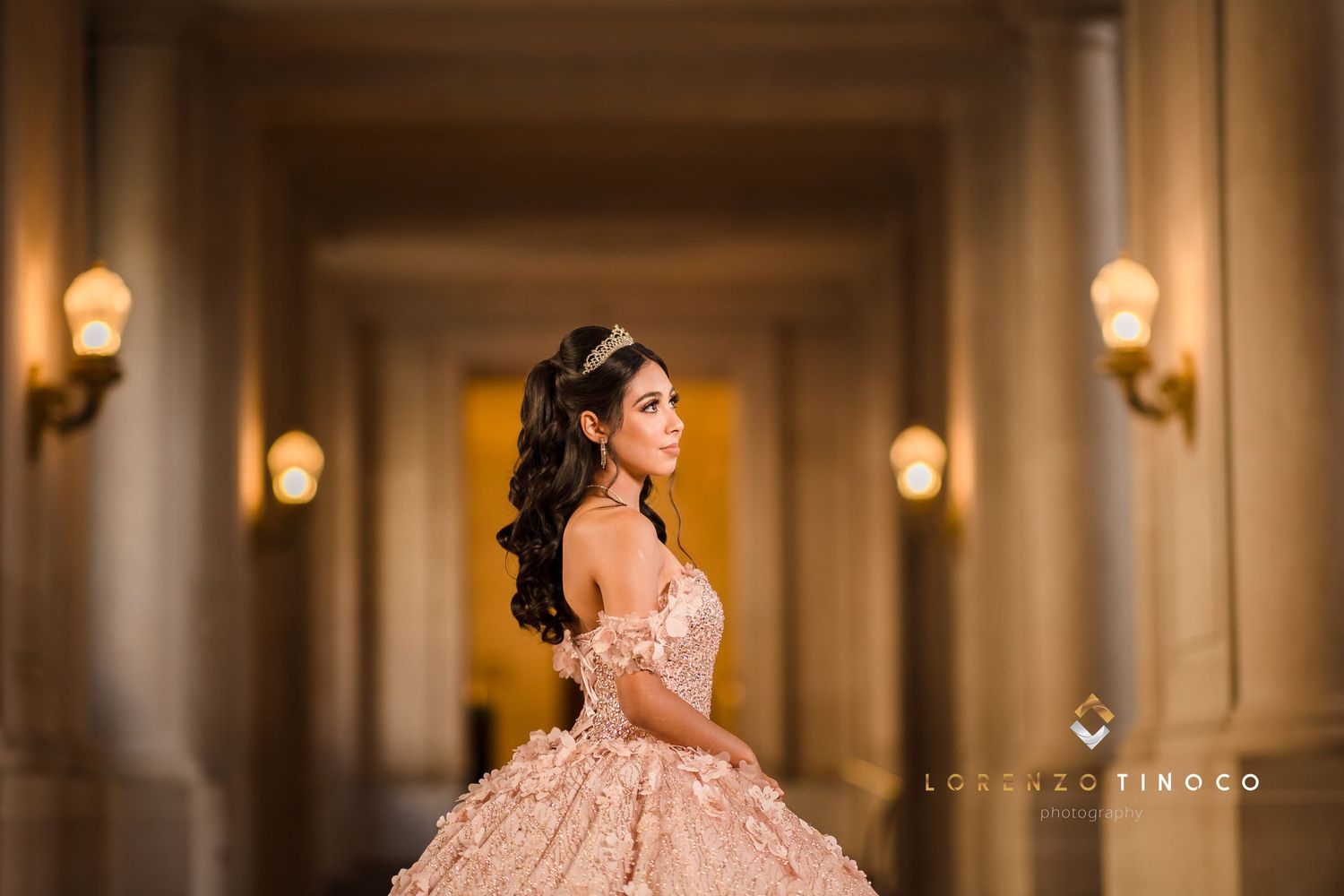 A romantic off-shoulder ball gown captured in a warmly lit hallway with wall sconces.