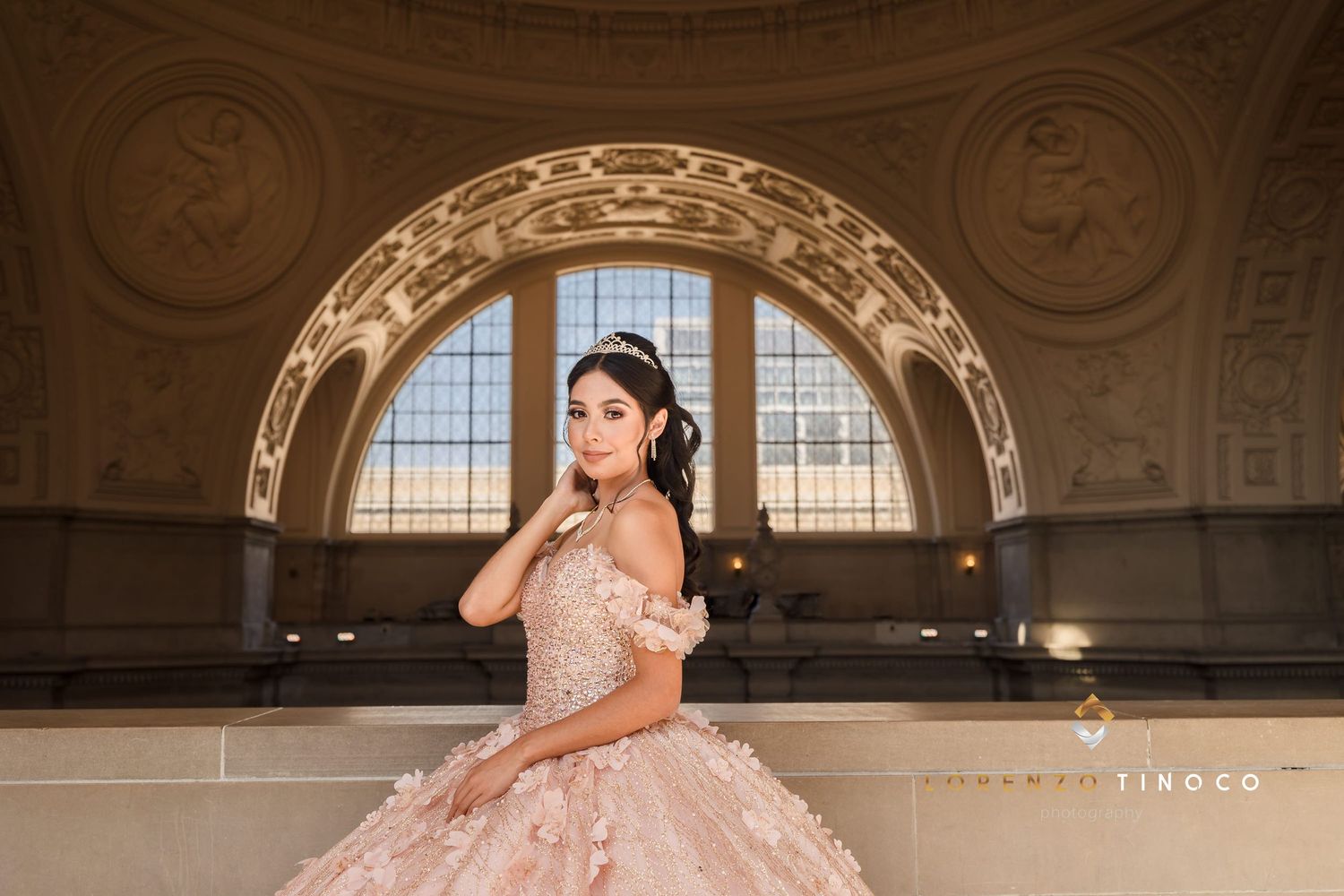 An elaborate pink ball gown photographed under an ornate domed ceiling with arched windows.
