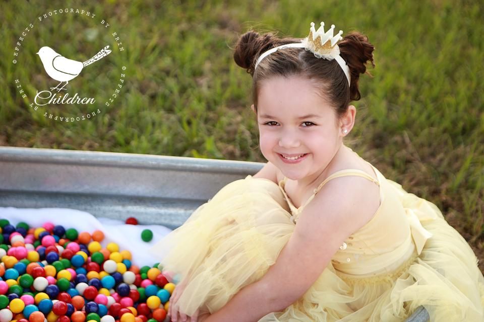 Child in yellow dress sitting by colorful ball pit outdoors.