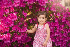 A child in a floral dress standing in front of vibrant pink bougainvillea flowers.