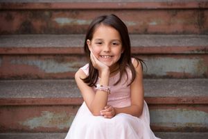 A child sitting on rustic wooden steps wearing a pink dress.