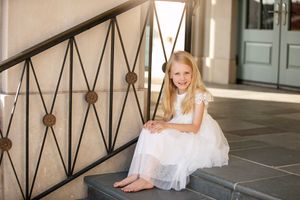 A child in a white tulle dress sitting on stone steps near a decorative railing.