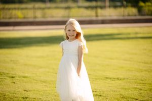 Portrait of child in flowing white dress standing in sunny meadow.