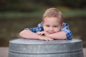 Portrait of youth in plaid shirt resting on metal barrel outdoors.