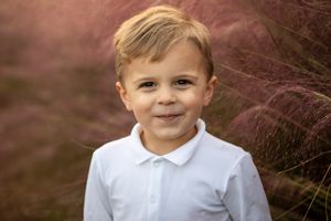 Portrait of young person in white polo shirt against blurred purple background.