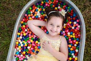 Overhead shot of person lying in tub filled with colorful ball pit balls wearing yellow dress.