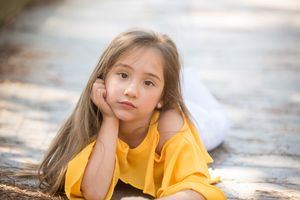 Portrait of person in yellow shirt lying on ground with contemplative expression.