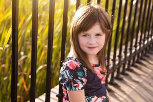 Portrait of person in floral dress standing by metal fence in golden sunlight.