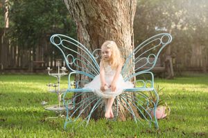 Magical fairy-themed portrait in a sunlit garden with ethereal blue digital wing effects.