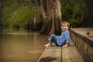 Waterfront portrait on wooden boardwalk beside cypress trees.