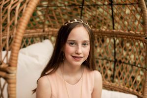 Portrait in peachy pink dress against woven wicker chair background.