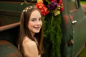 Portrait in peach colored top against vintage truck with colorful floral decorations.