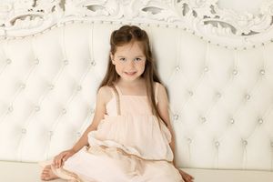 Portrait on white tufted furniture in flowing blush dress.