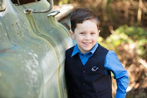Child in formal attire smiles while leaning against a turquoise surface outdoors.