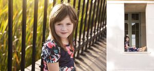 Portrait against iron fence with sunlit foliage in background.