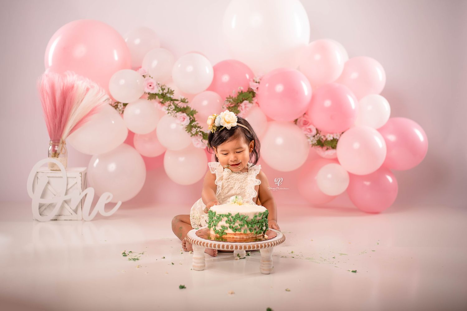 One year old baby girl eating cake for birthday photos, pink & white balloons with leaves; South Carolina photographer