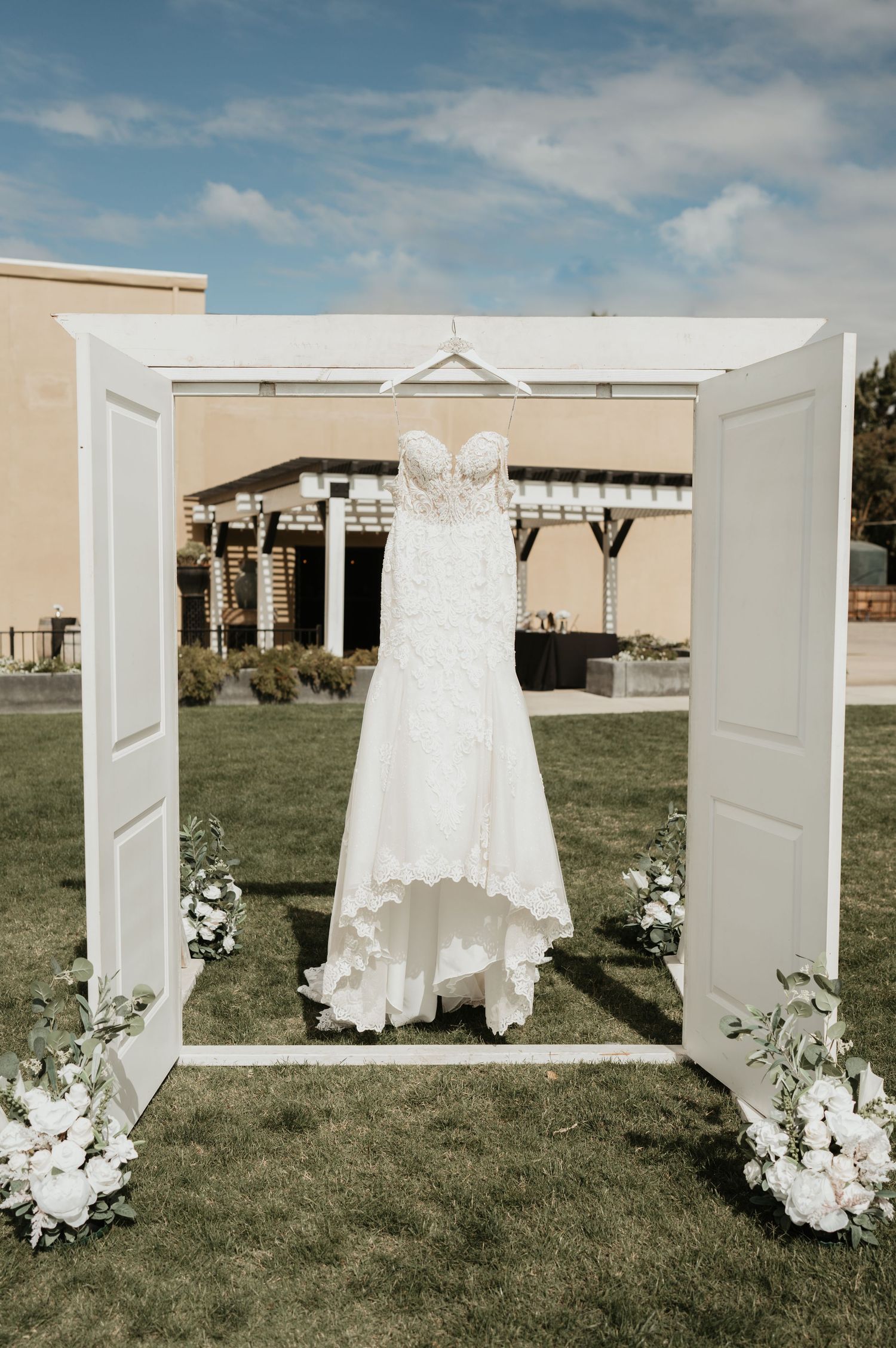 An elegant white lace wedding dress displayed on a decorated white door frame with floral accents.