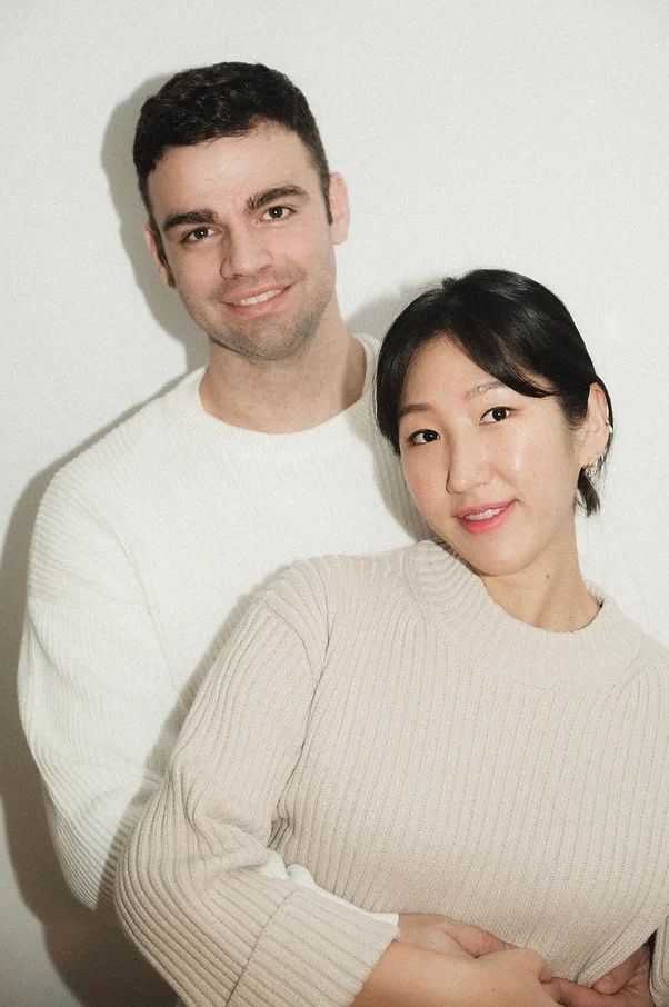 Indoor portrait of couple in cream-colored sweaters against white wall.