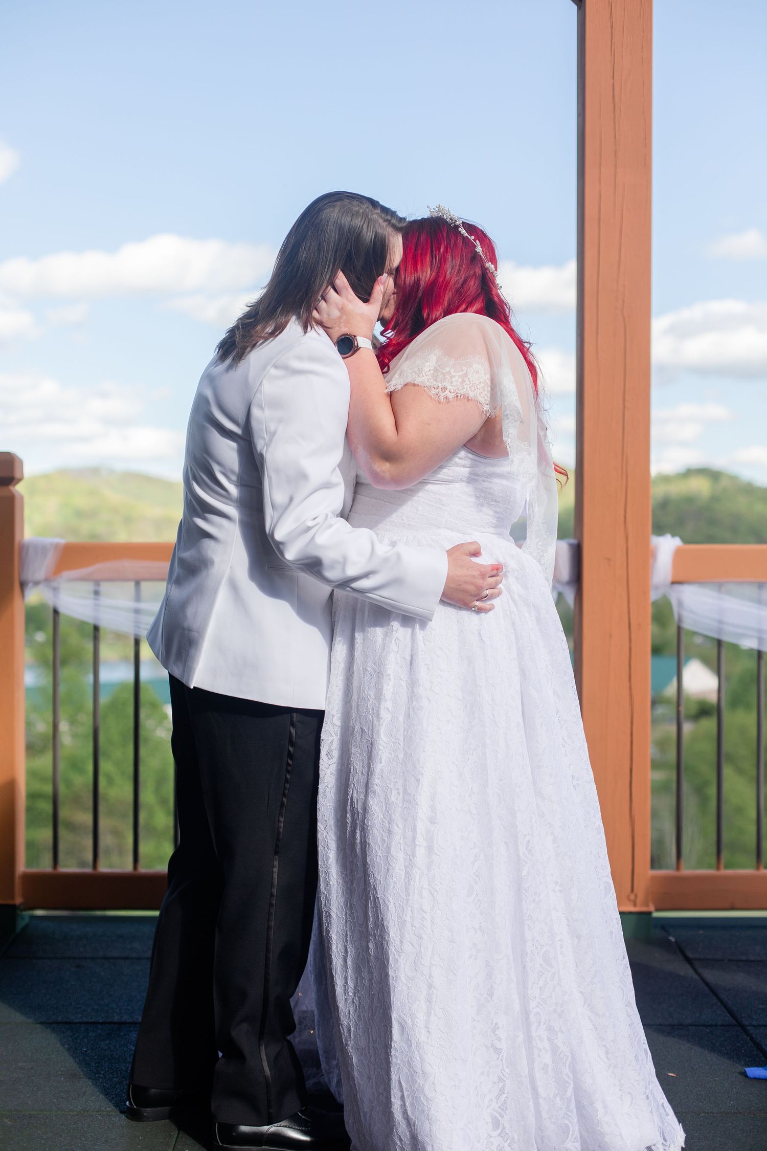 Wedding couple embraces on a scenic outdoor deck with mountain views.