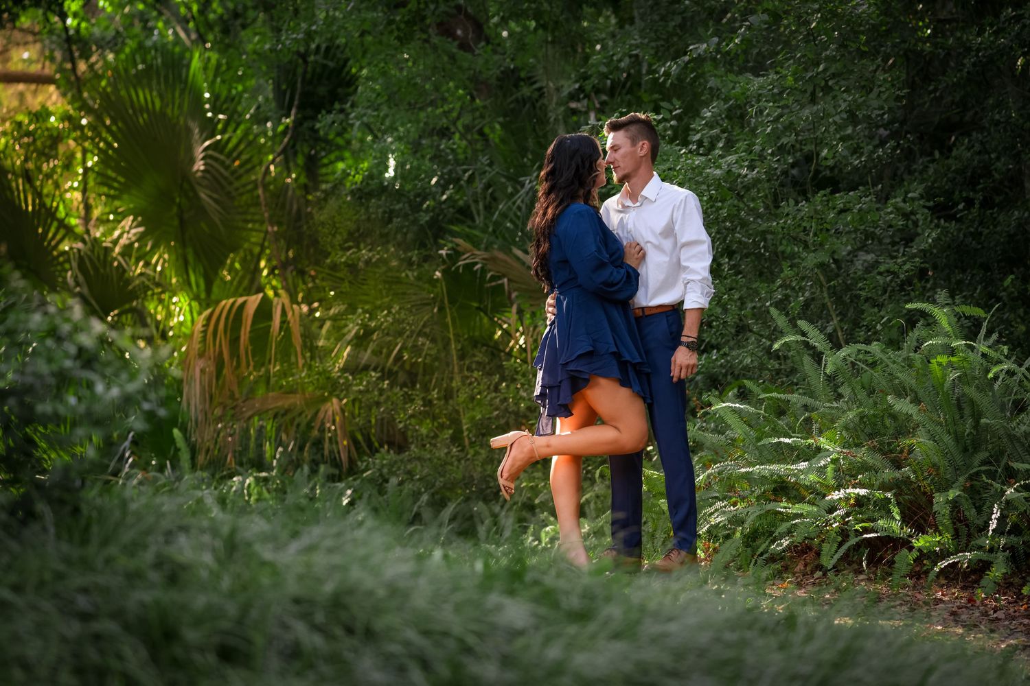 Romantic engagement portrait in lush garden setting during golden hour.