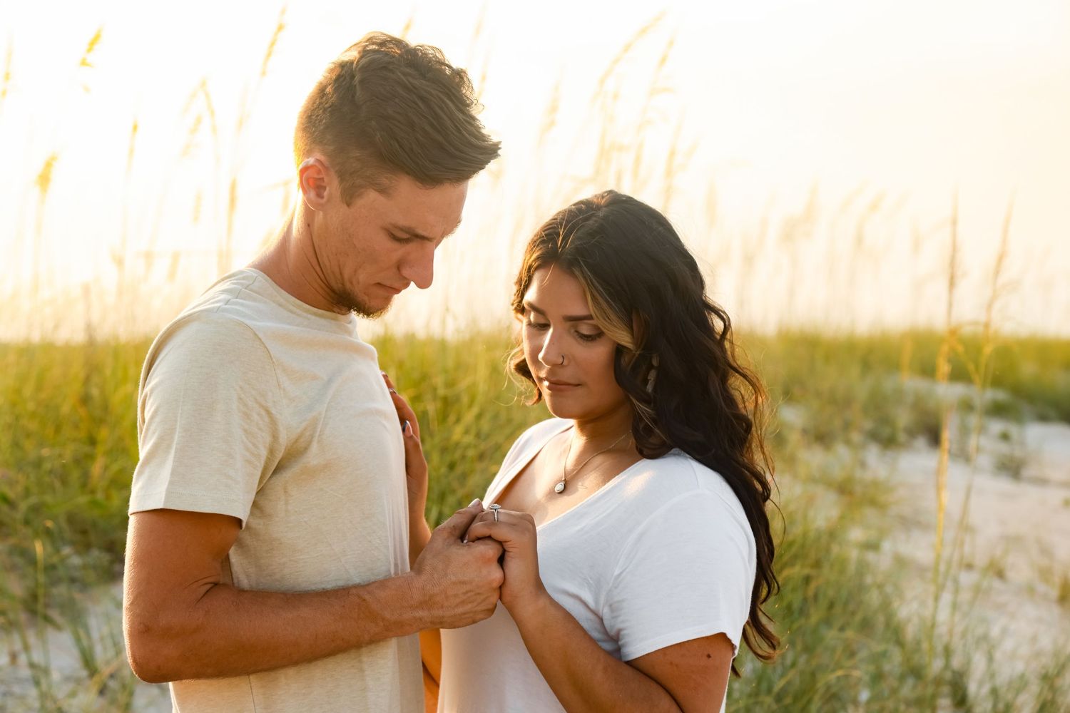 A couple shares an intimate moment together in tall grass during golden hour lighting.