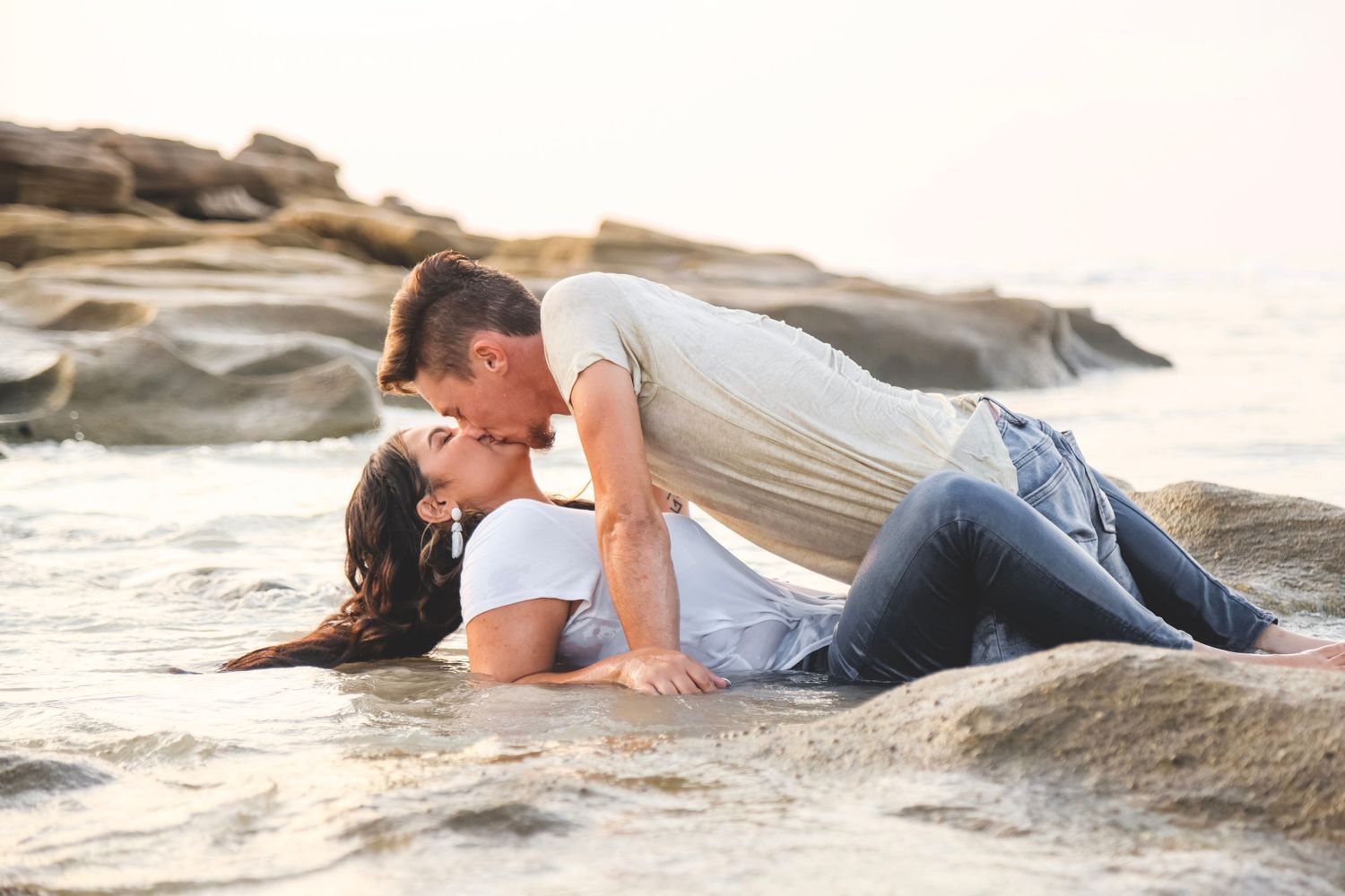 A romantic moment captured on rocky coastal terrain with ocean waves in the background.
