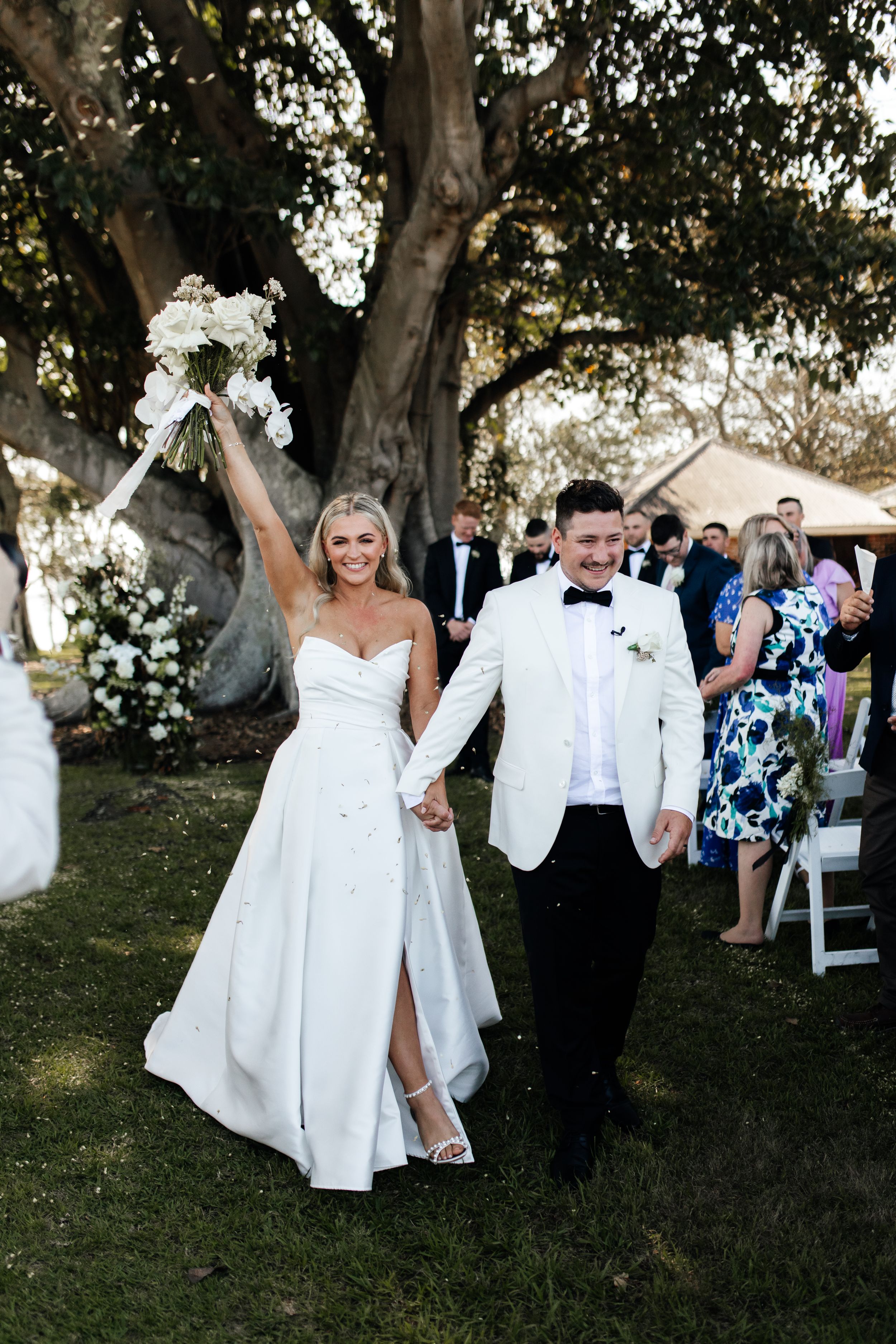 A wedding couple walks down the aisle together while guests cheer in an outdoor garden ceremony.
