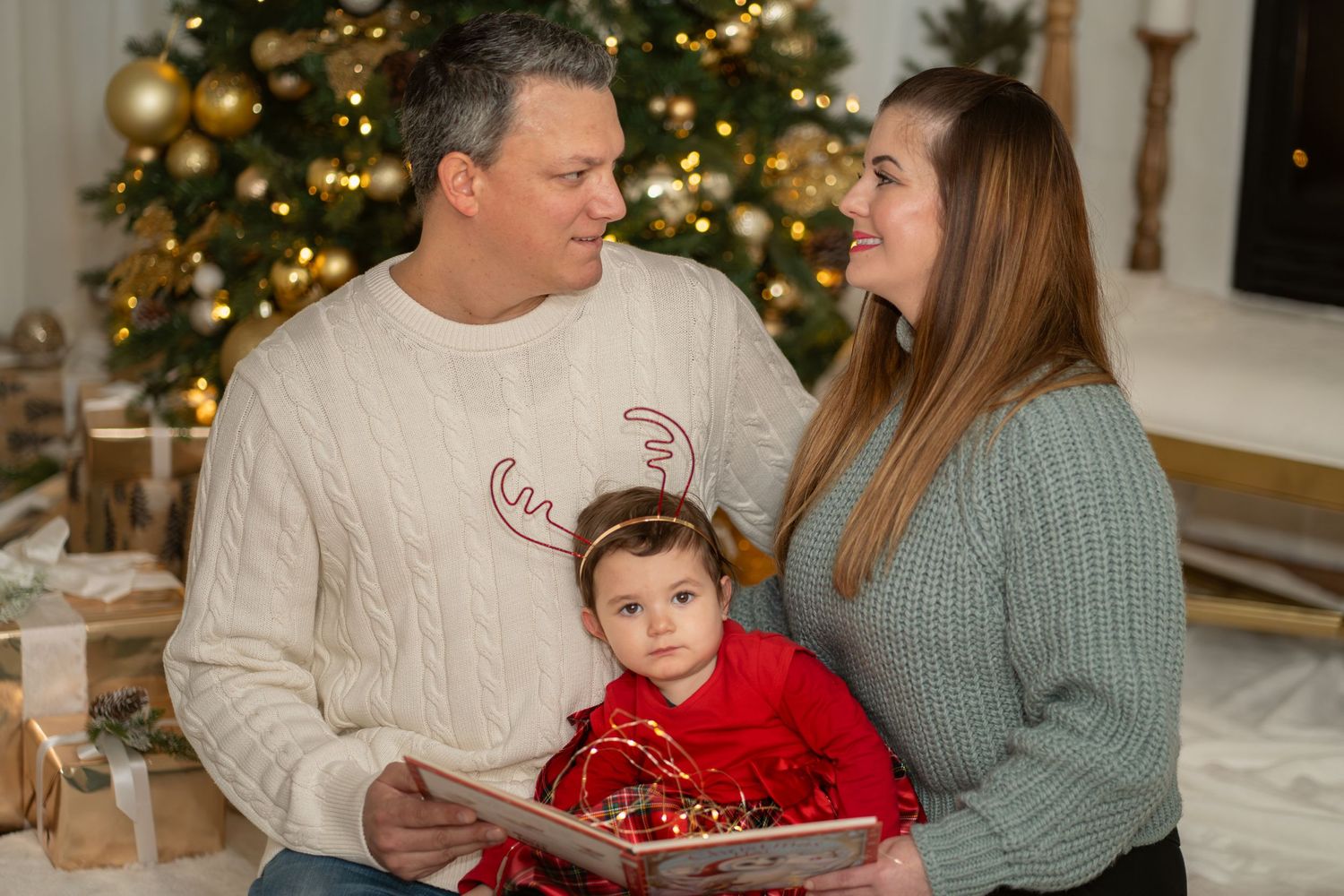 Family in cozy sweaters reads holiday story together near decorated Christmas tree.