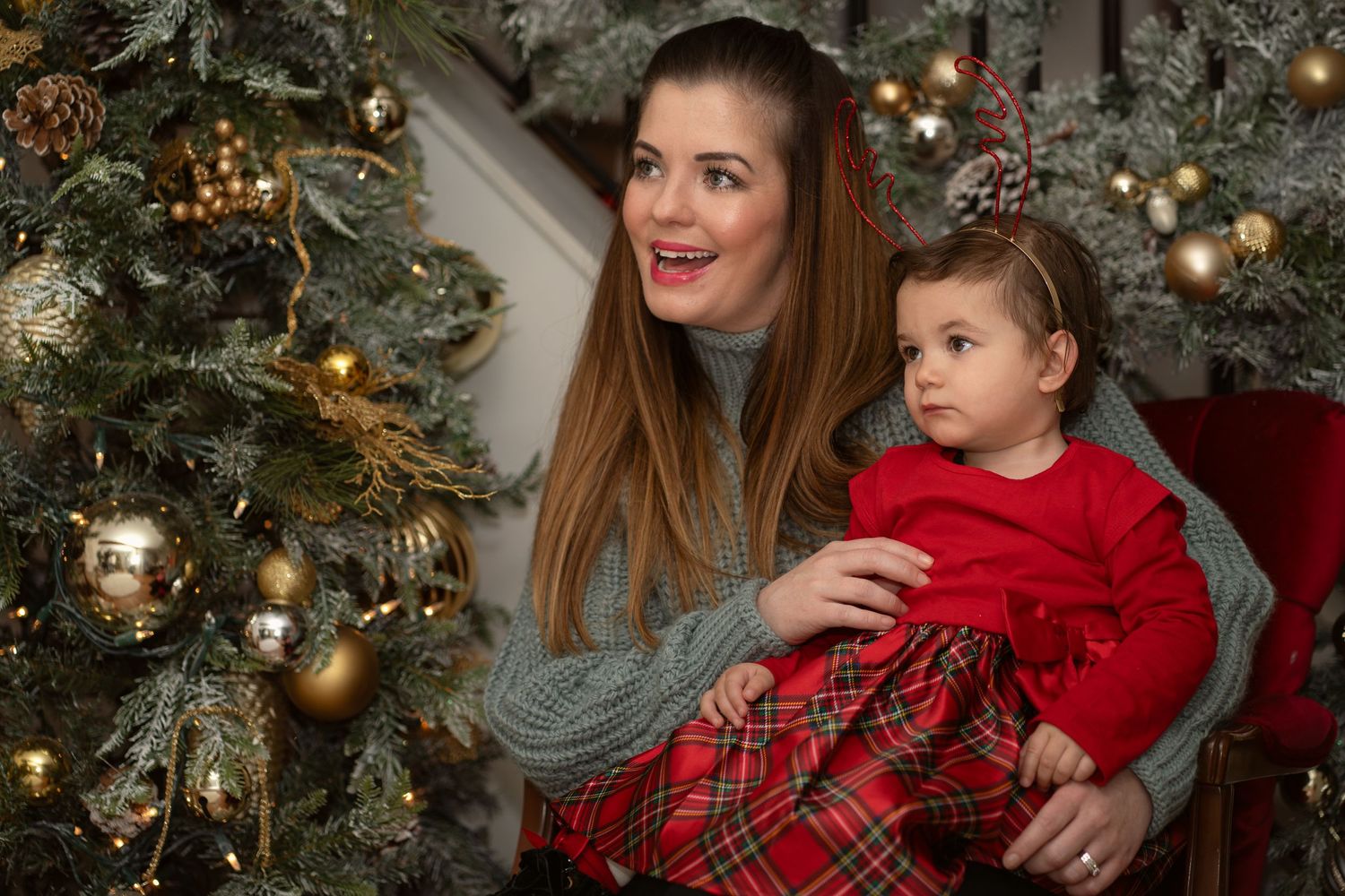 Family portrait with festive outfits and decorated Christmas tree in background.