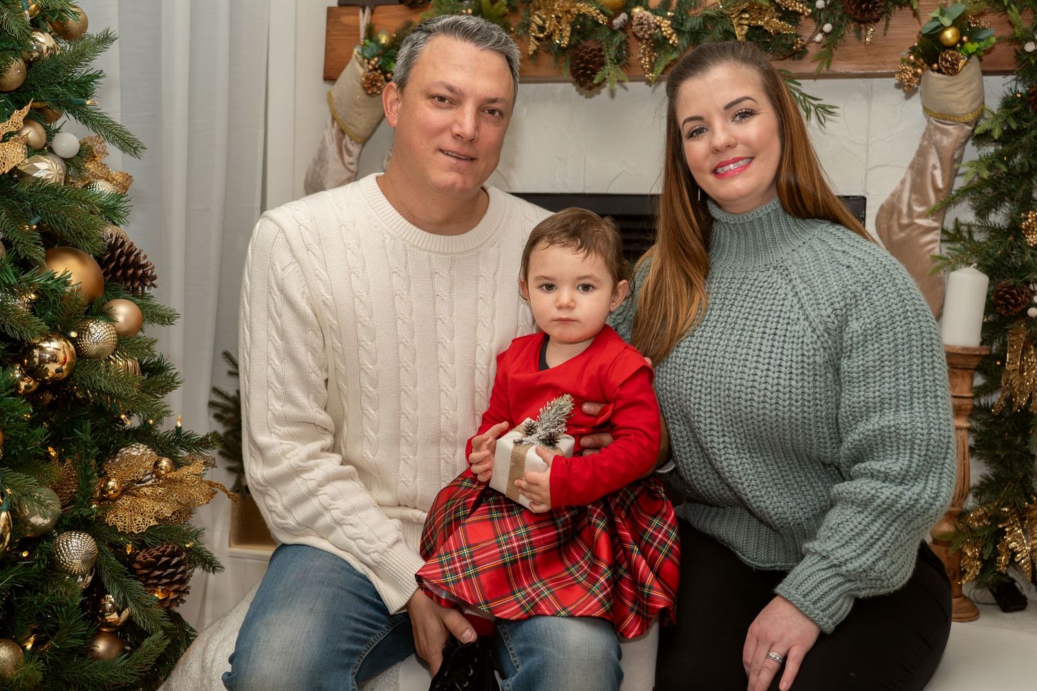 Holiday family portrait with coordinated sweaters in front of Christmas tree.