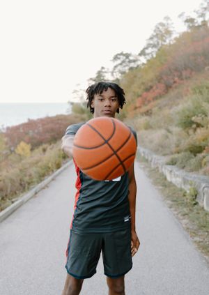 Basketball player holding ball on outdoor path with autumn scenery.