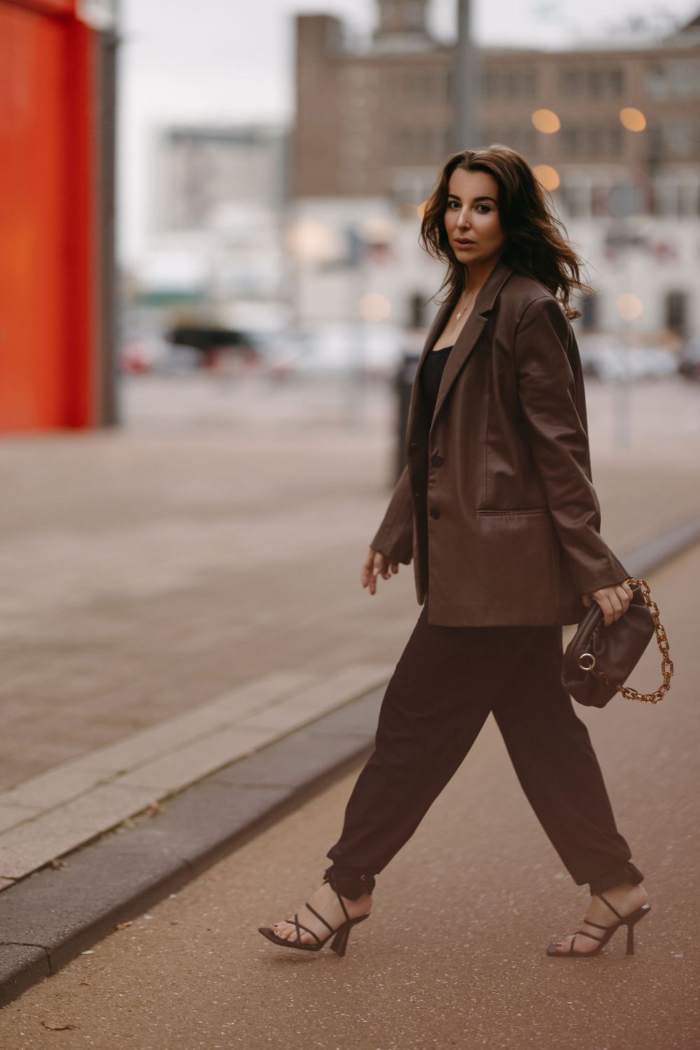 Street style photo showing brown blazer outfit with chain handle bag in urban setting.