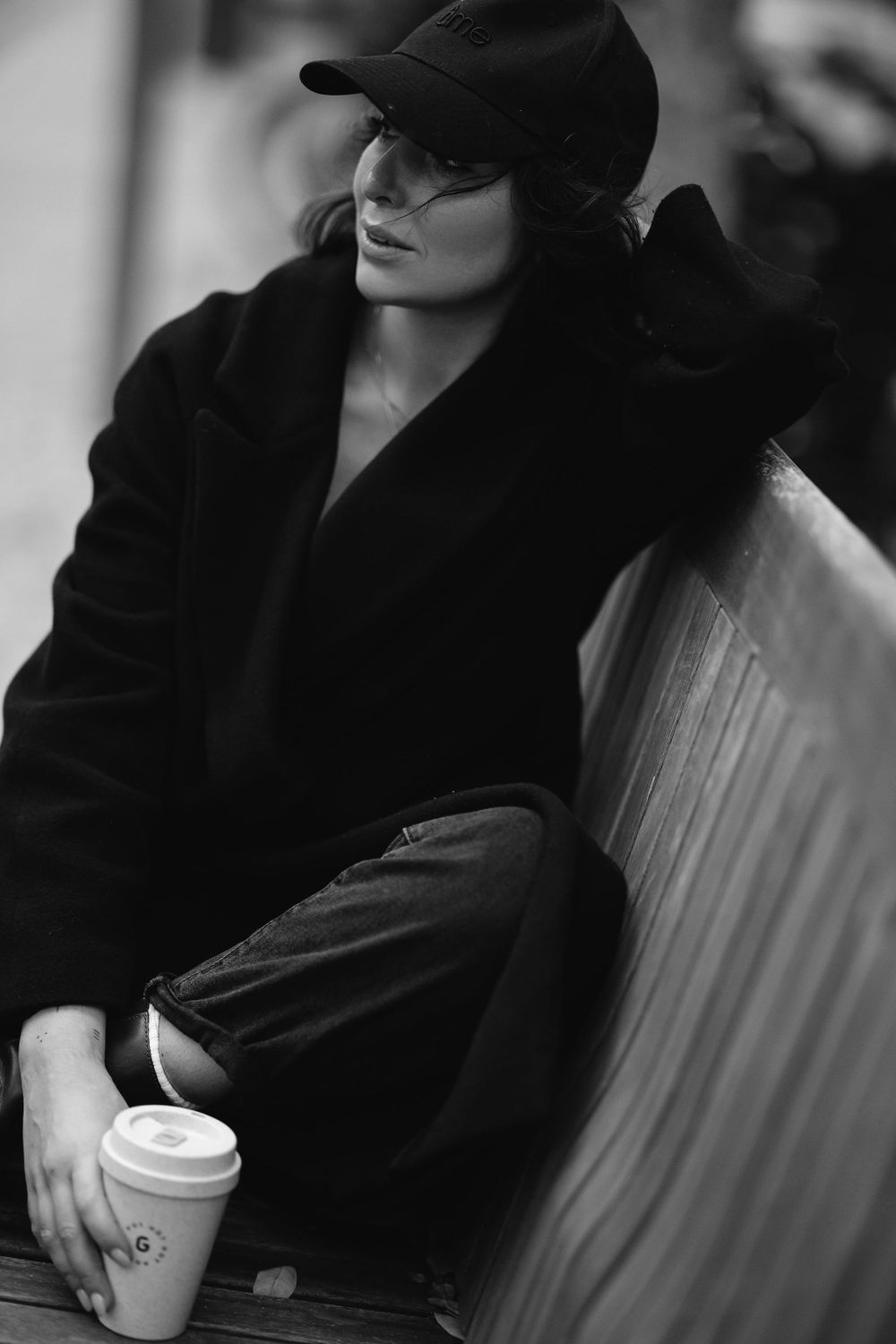 Moody black and white portrait of street style fashion with baseball cap and coffee cup.