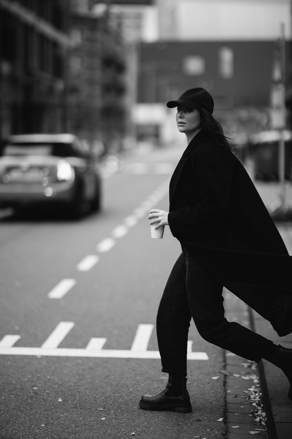 Dynamic street fashion photograph capturing movement in all-black urban outfit with baseball cap.