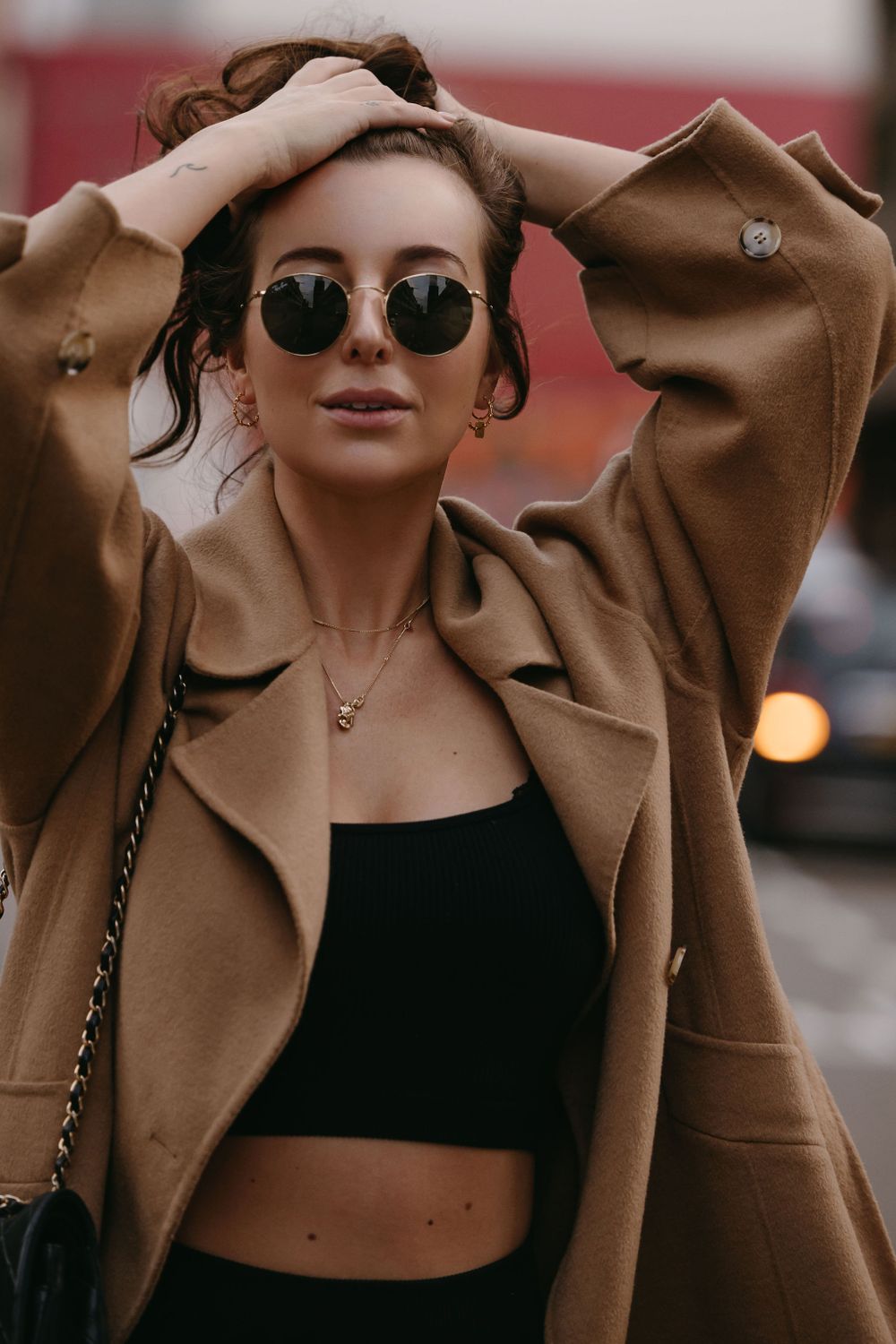 Fashionable street style with camel coat, crop top and round sunglasses in urban setting.