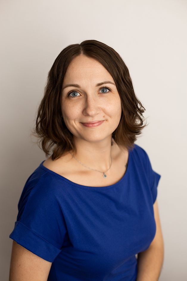 Woman on white backdrop wearing blue dress smiling at the camera.