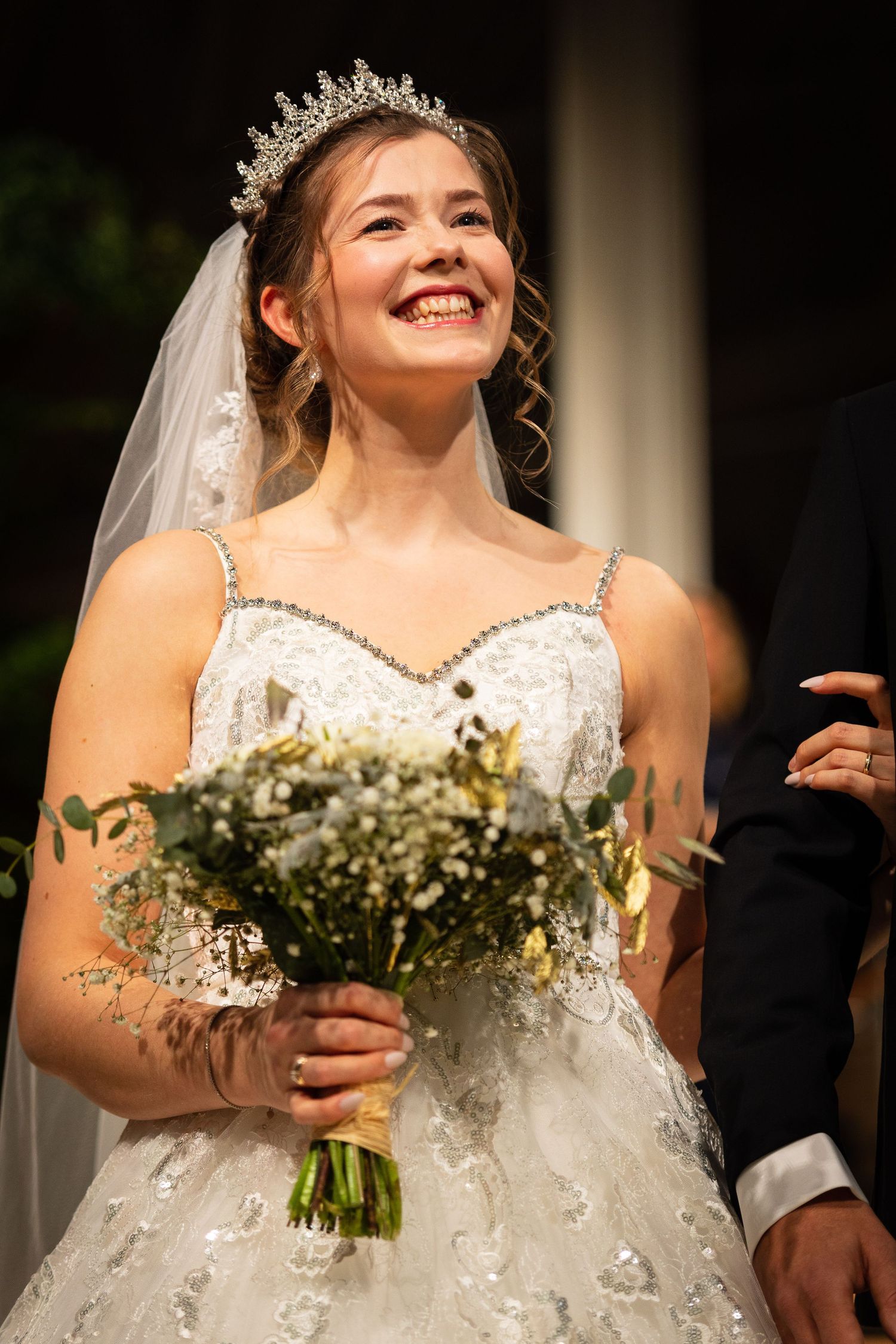 Joyful bride wearing a tiara and veil holding a white wildflower bouquet at her wedding.
