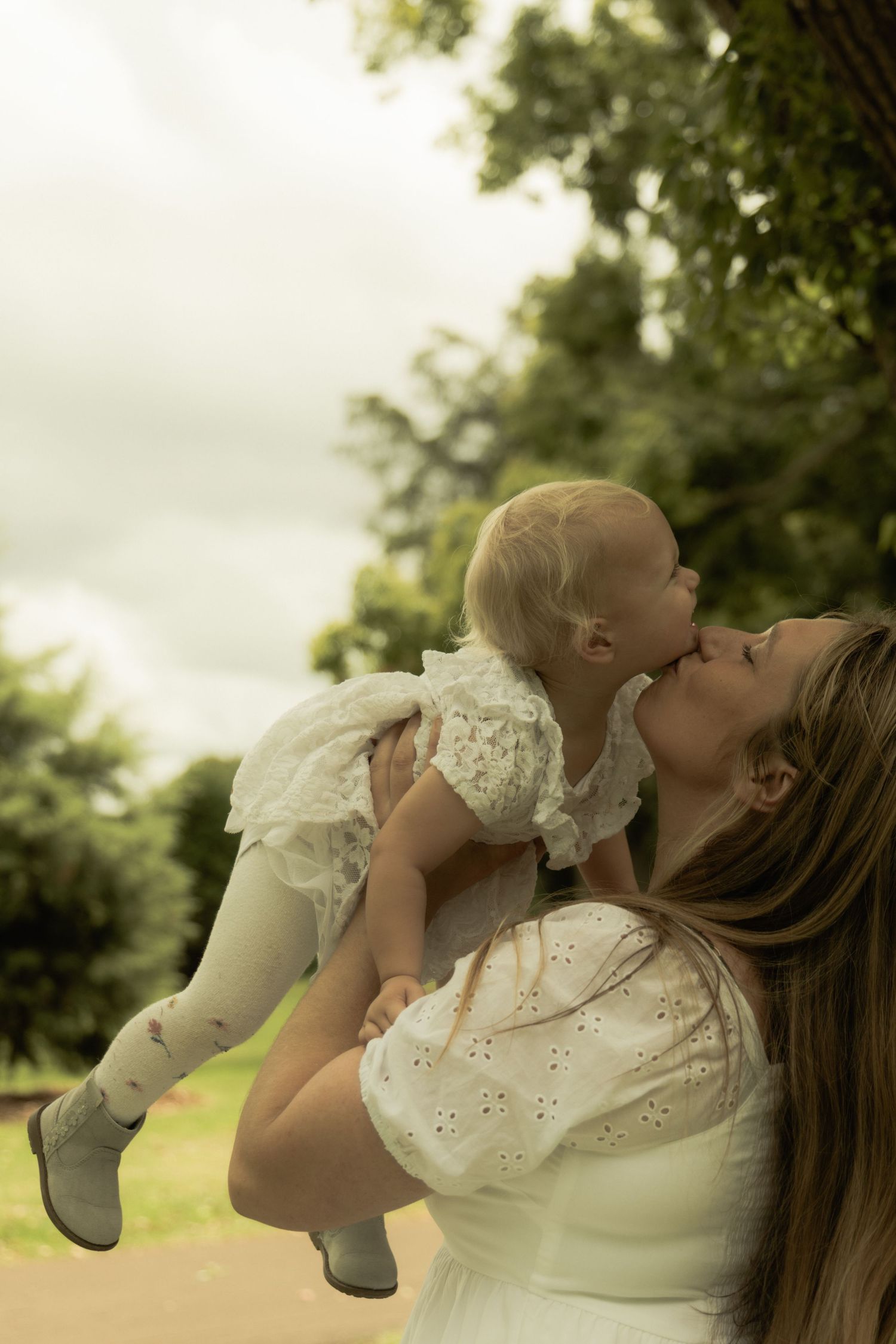 A touching maternal moment outdoors with soft natural lighting and lace details.