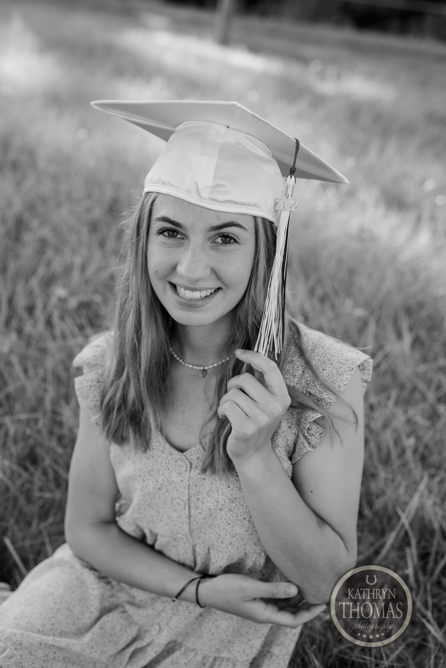 Black and white portrait of graduate in cap and gown smiling in outdoor setting.
