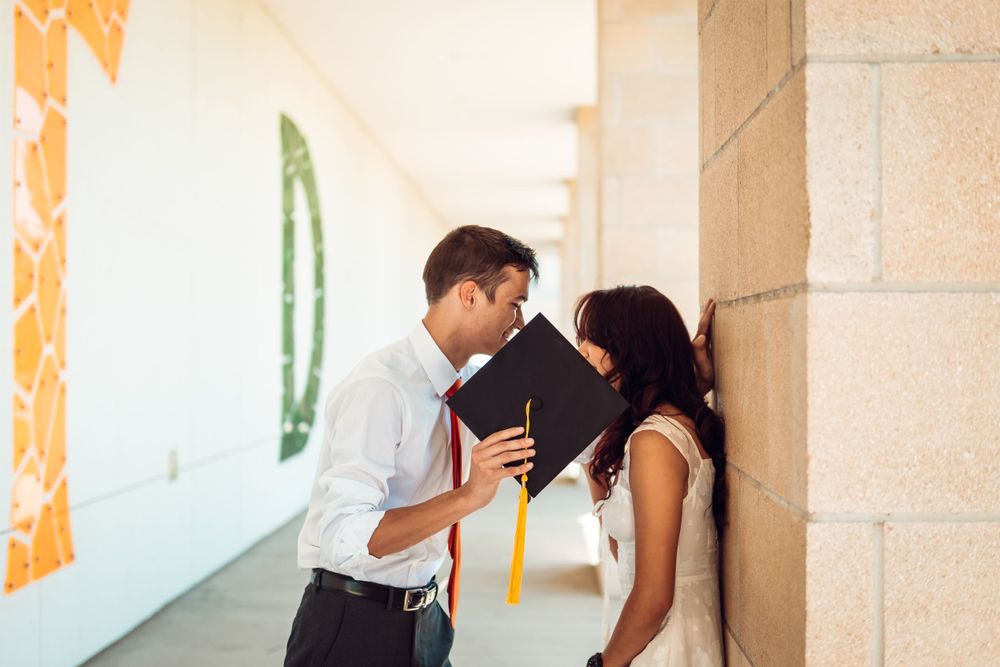 Couple in formal wear pose playfully against beige wall with orange decorative elements.