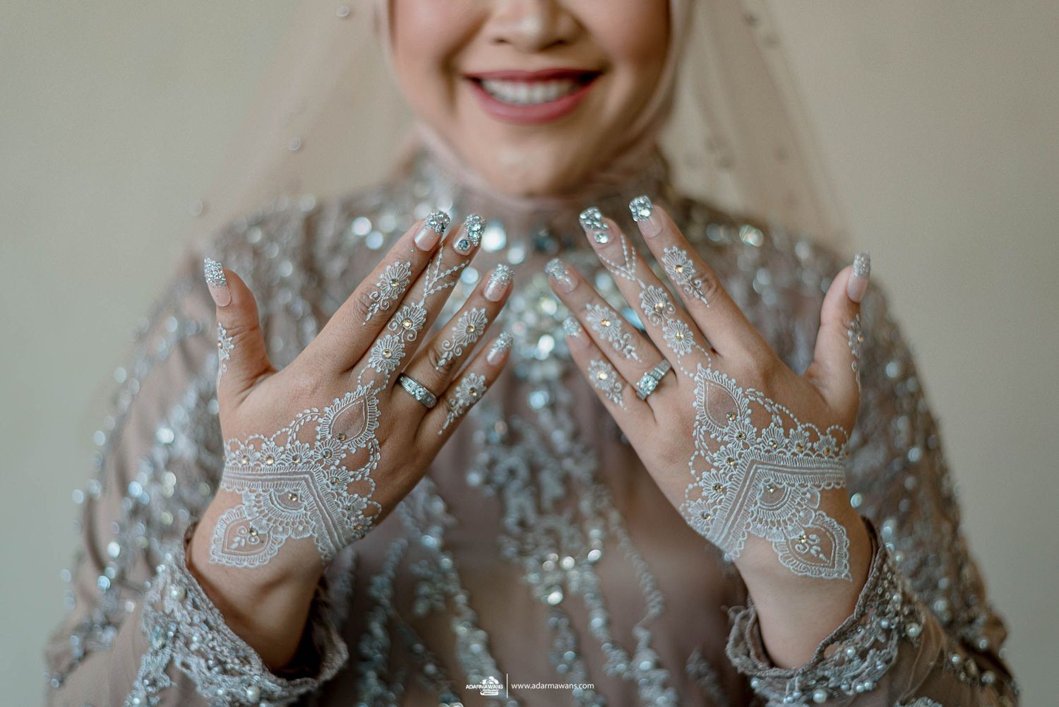 Beautiful white henna designs decorate hands adorned with rings and sparkly embellishments.