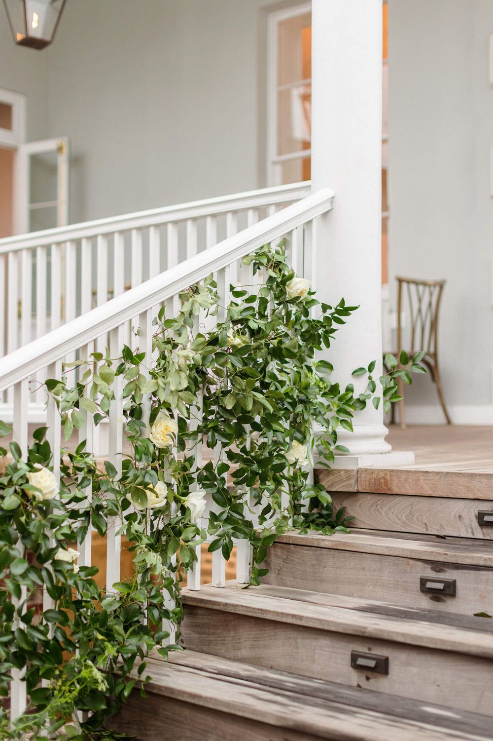 Elegant white staircase decorated with lush green foliage and white flowers for a wedding ceremony.