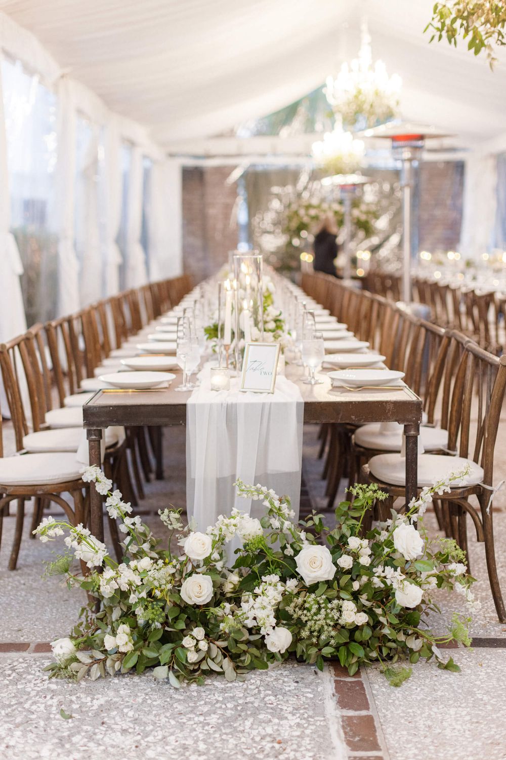 Rustic elegant wedding reception table with white linens and floral arrangements in a tented space.