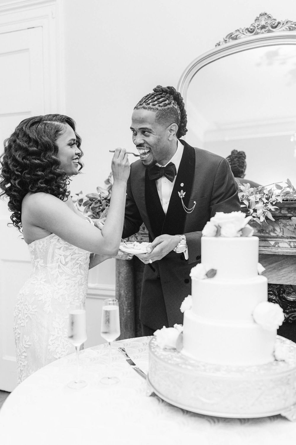 A couple playfully shares cake during their wedding reception beside their elegant tiered cake.