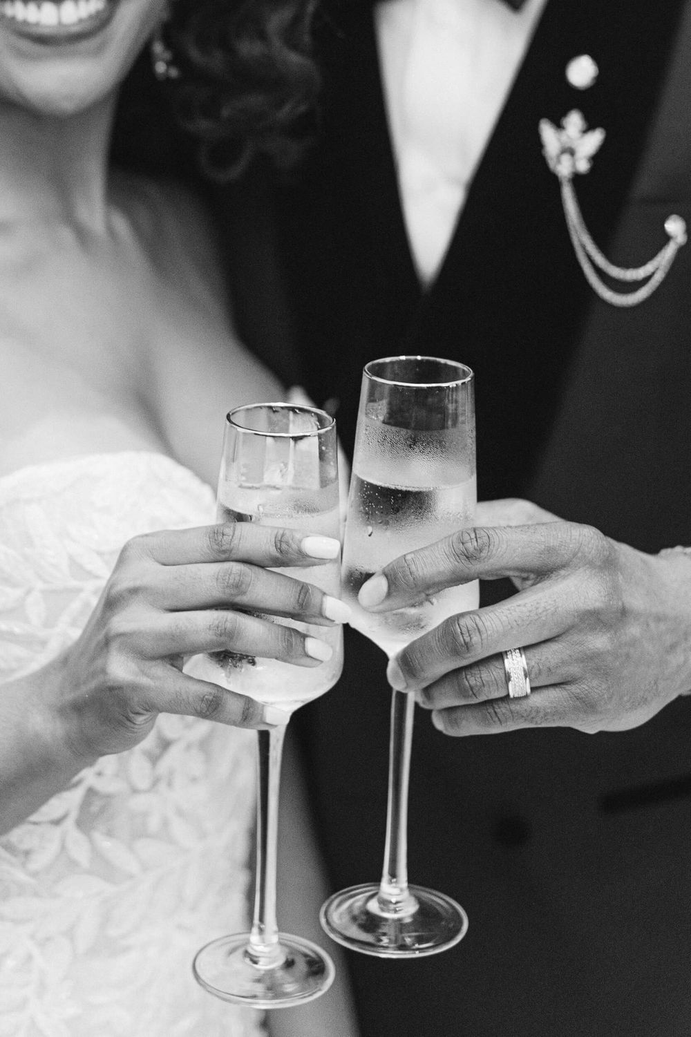 Close-up of newlyweds toasting with champagne flutes, showing wedding rings and formal attire.
